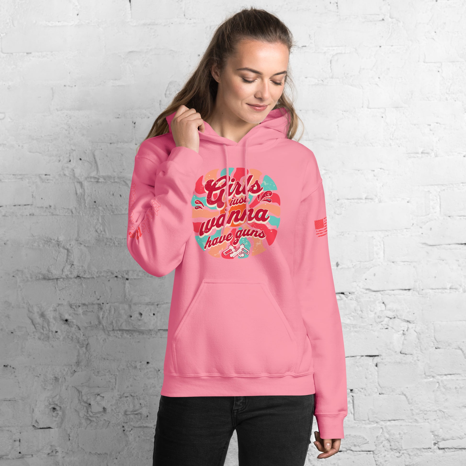 Person wearing a pink hoodie with colorful text design against a white brick wall.