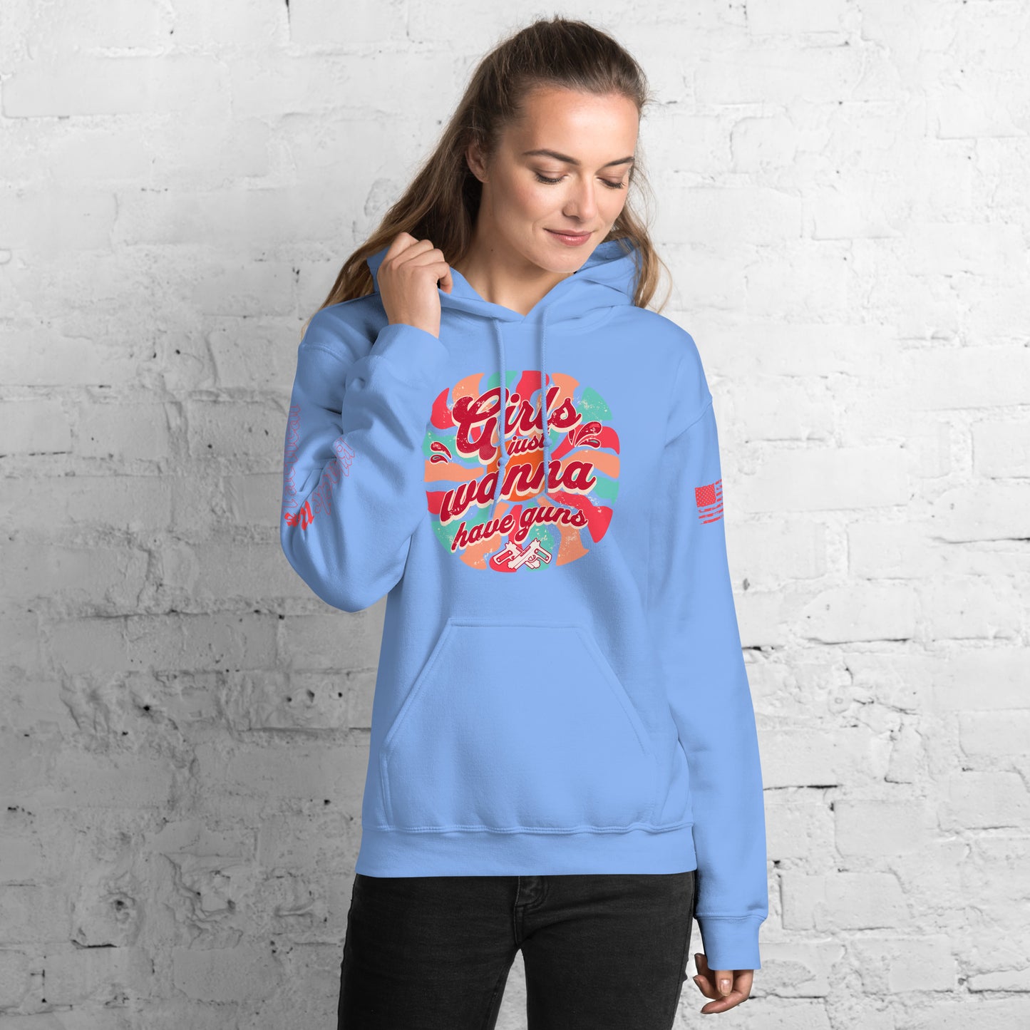 Woman wearing a light blue hoodie with colorful text design against a white brick wall.