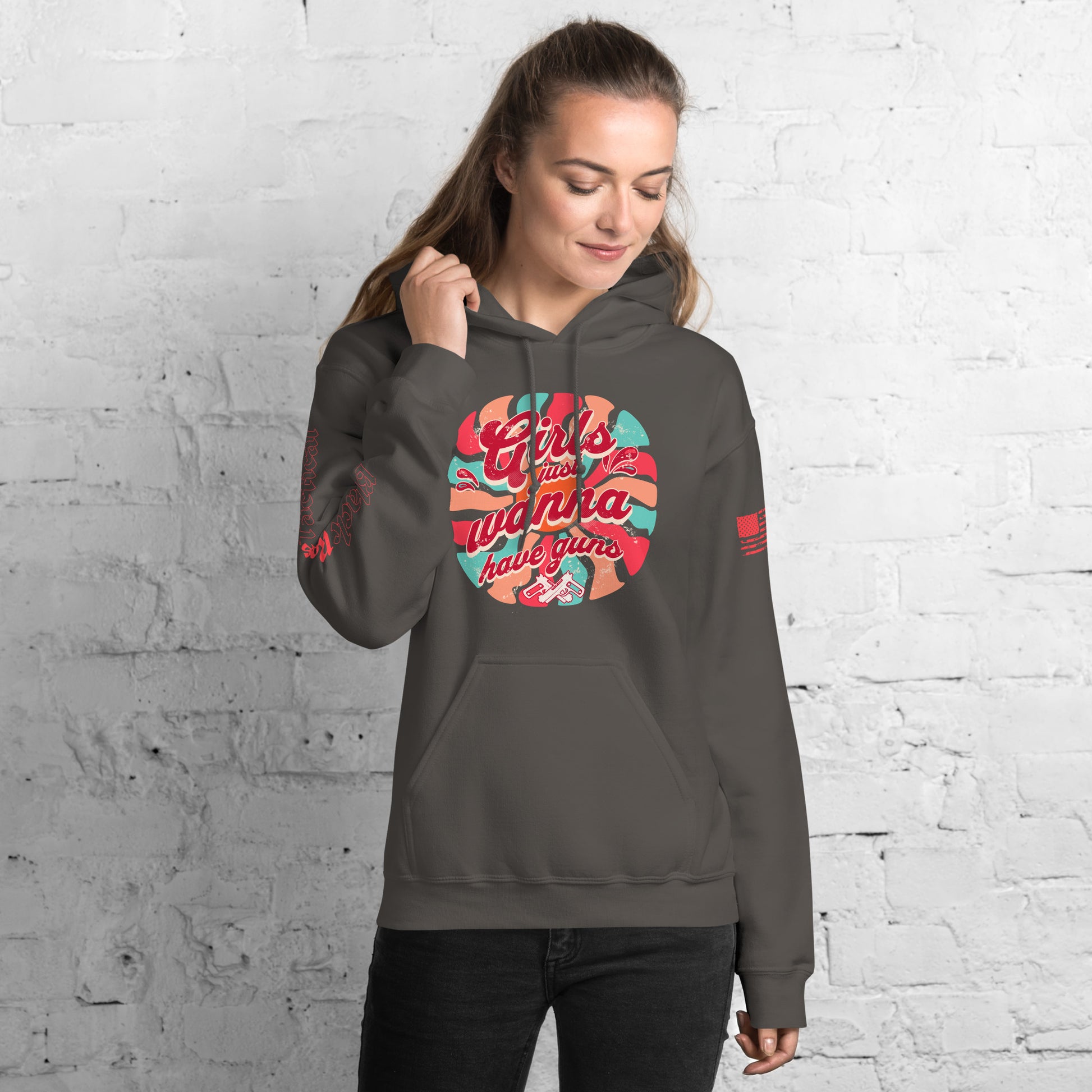 Woman wearing a gray hoodie with colorful graphic design against a white brick wall.