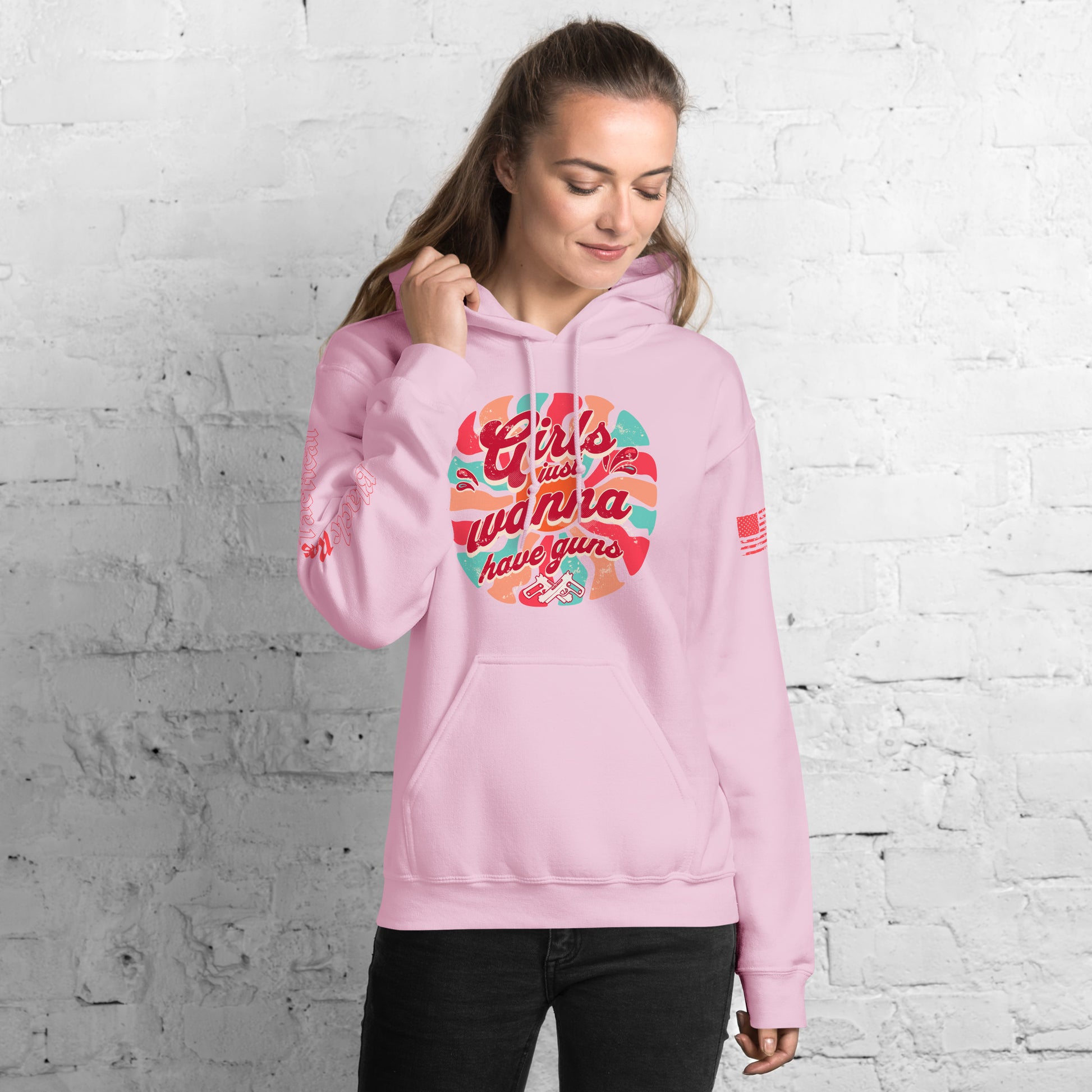 Woman wearing a pink hoodie with colorful text design against a white brick wall.
