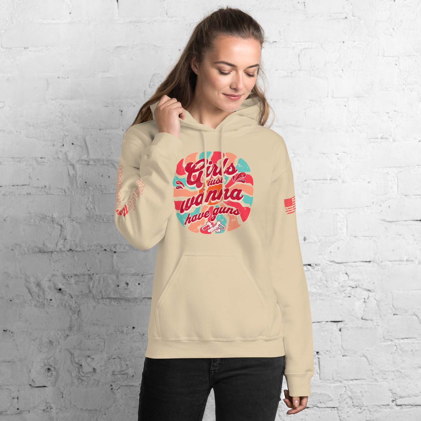Woman wearing a beige hoodie with colorful text design against a white brick wall.