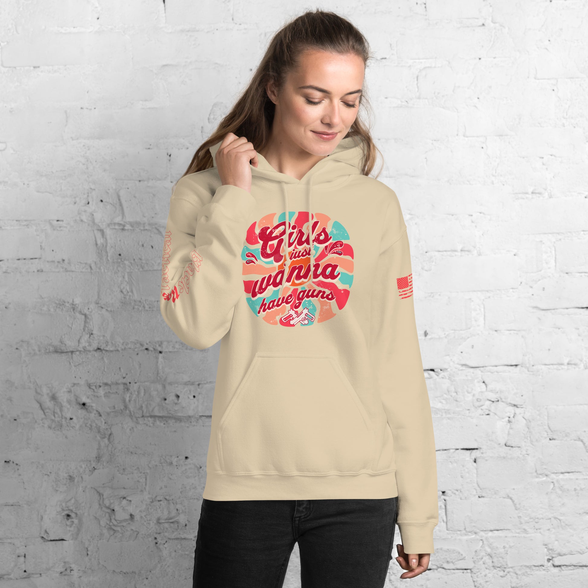 Woman wearing a beige hoodie with colorful text design against a white brick wall.