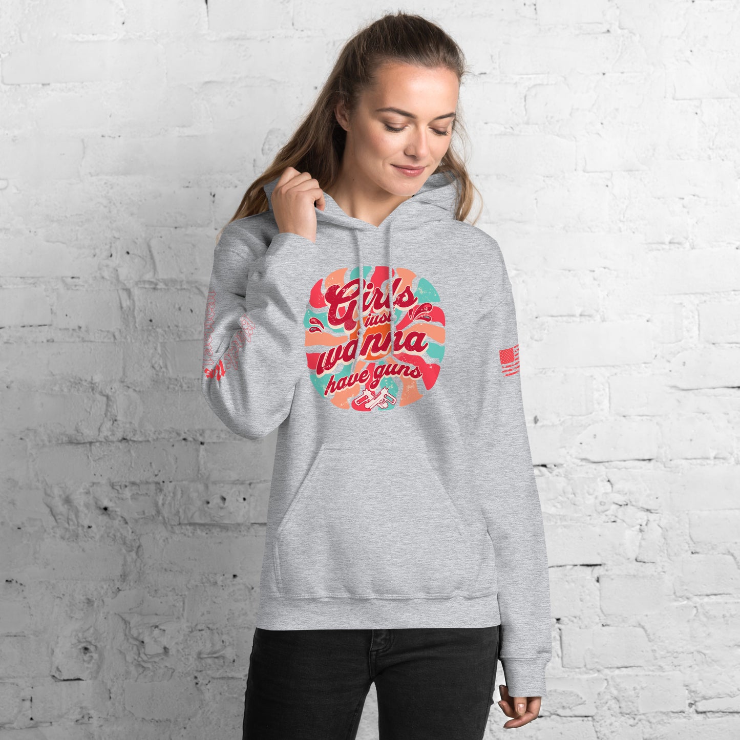 Woman wearing a gray hoodie with colorful graphic design against a white brick wall.
