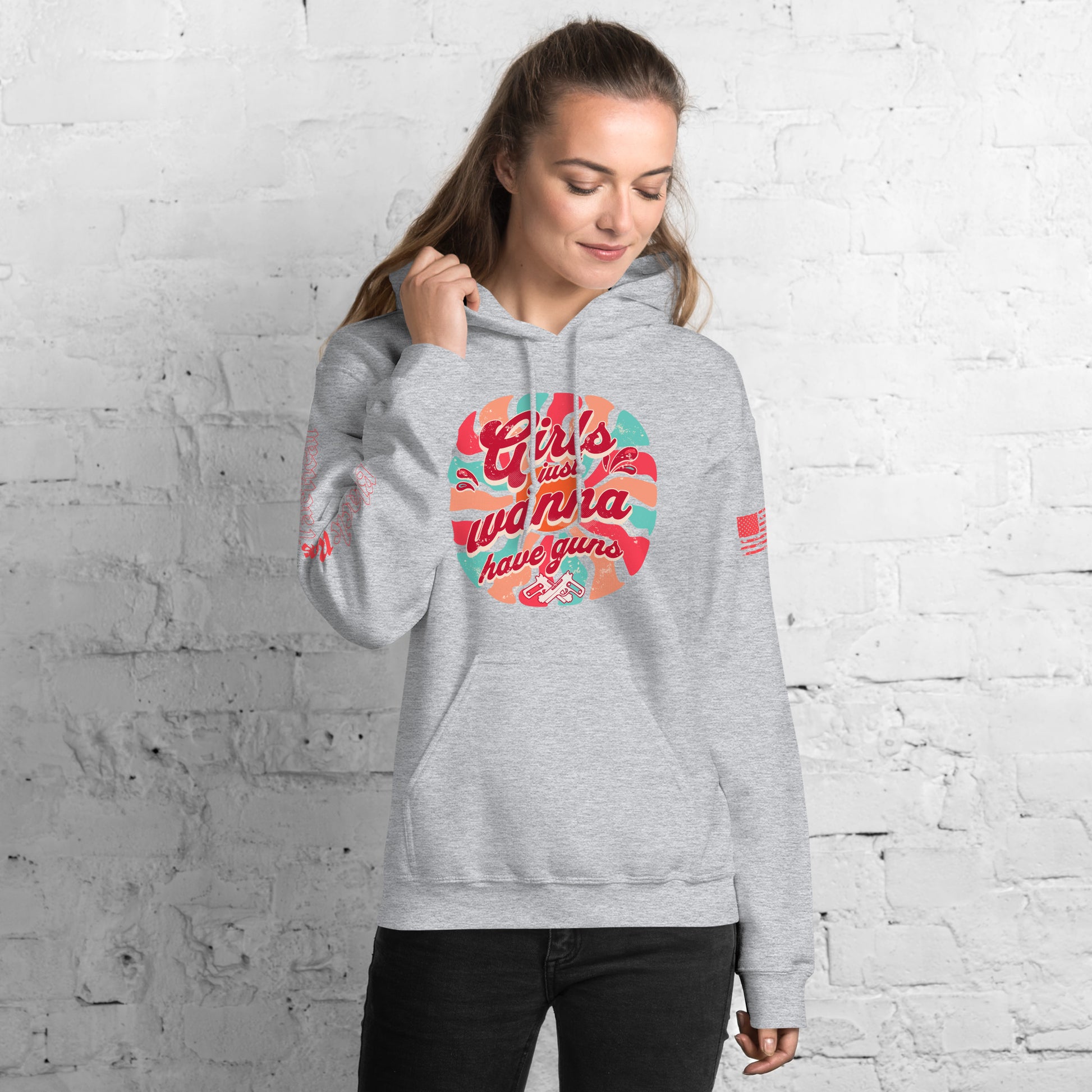 Woman wearing a gray hoodie with colorful graphic design against a white brick wall.