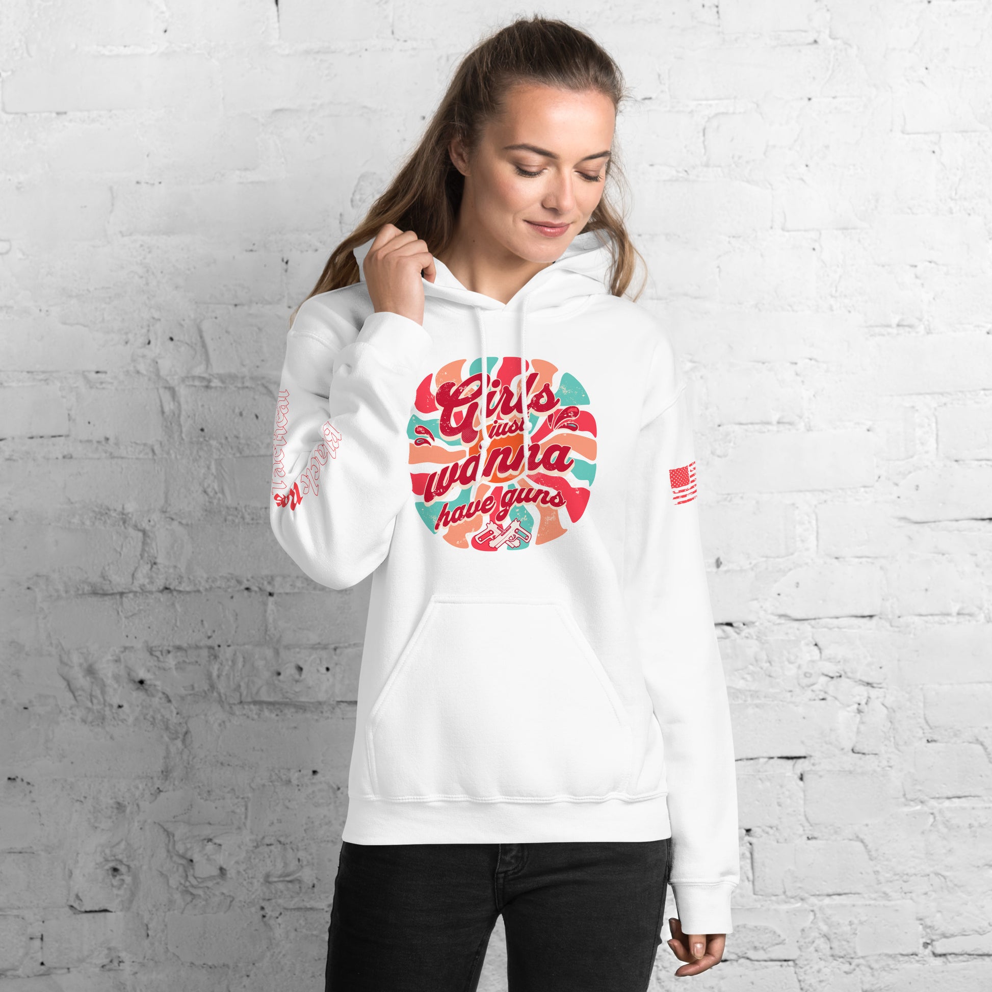 Woman wearing a white hoodie with colorful text design against a white brick wall.