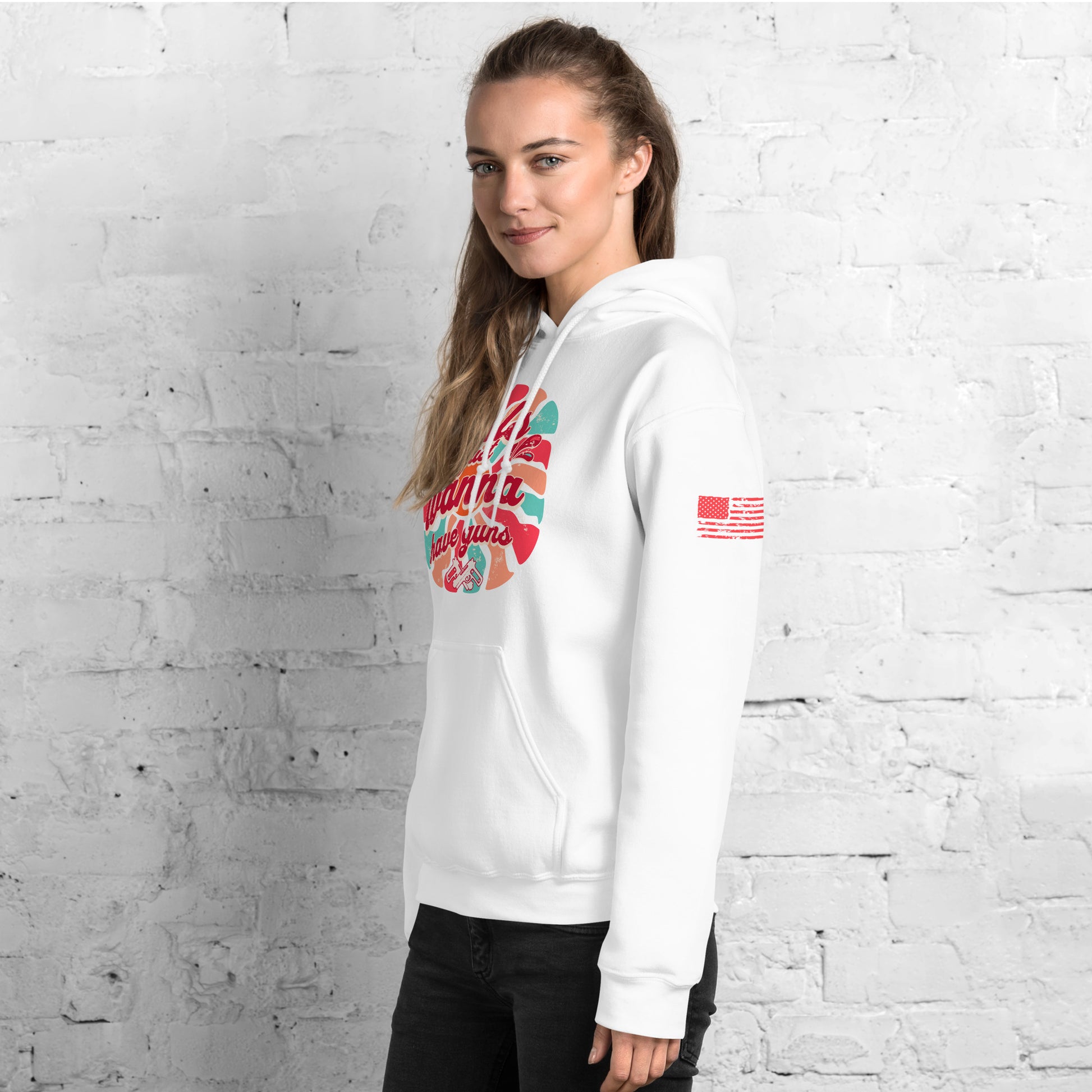 Person wearing a white hoodie with colorful graphics against a white brick wall American Flag on sleeve.