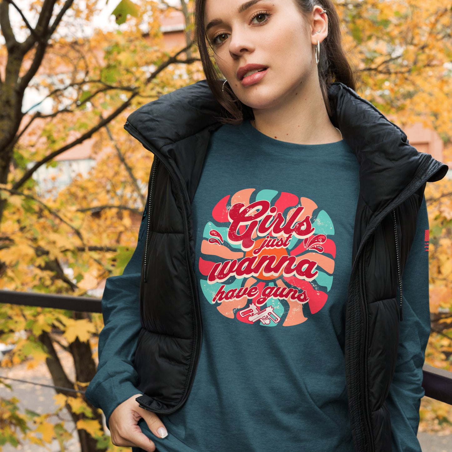 Woman wearing a teal t-shirt with colorful graphic design outdoors with autumn trees.