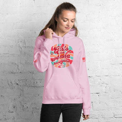 Woman wearing a pink hoodie with colorful text design against a white brick wall.