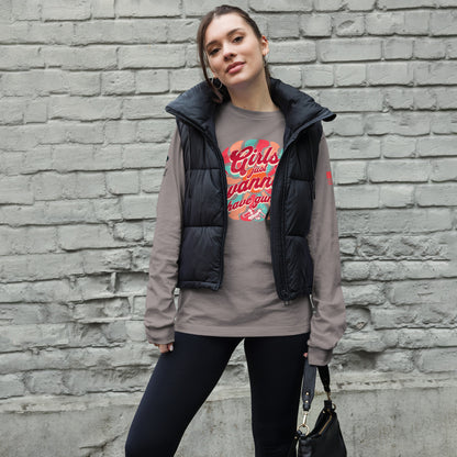 Woman wearing a gray long sleeve shirt with a black vest over a graphic t-shirt against a brick wall.
